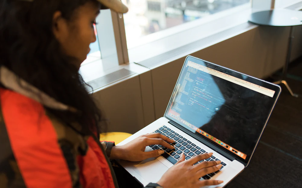 A woman by a window typing code on a laptop
